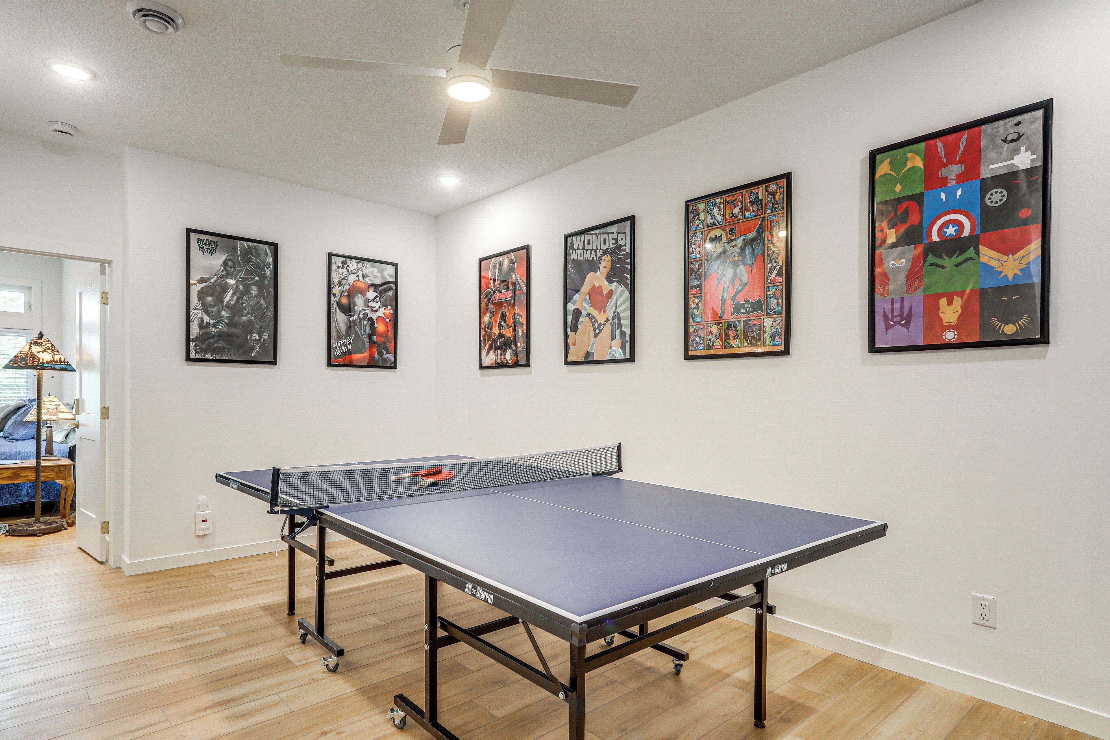 Une pièce équipée d’une table de ping-pong, d’un ventilateur de plafond et décorée avec des œuvres d’art mural.