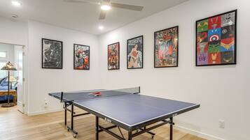 A room with a ping pong table, ceiling fan, and wall art.