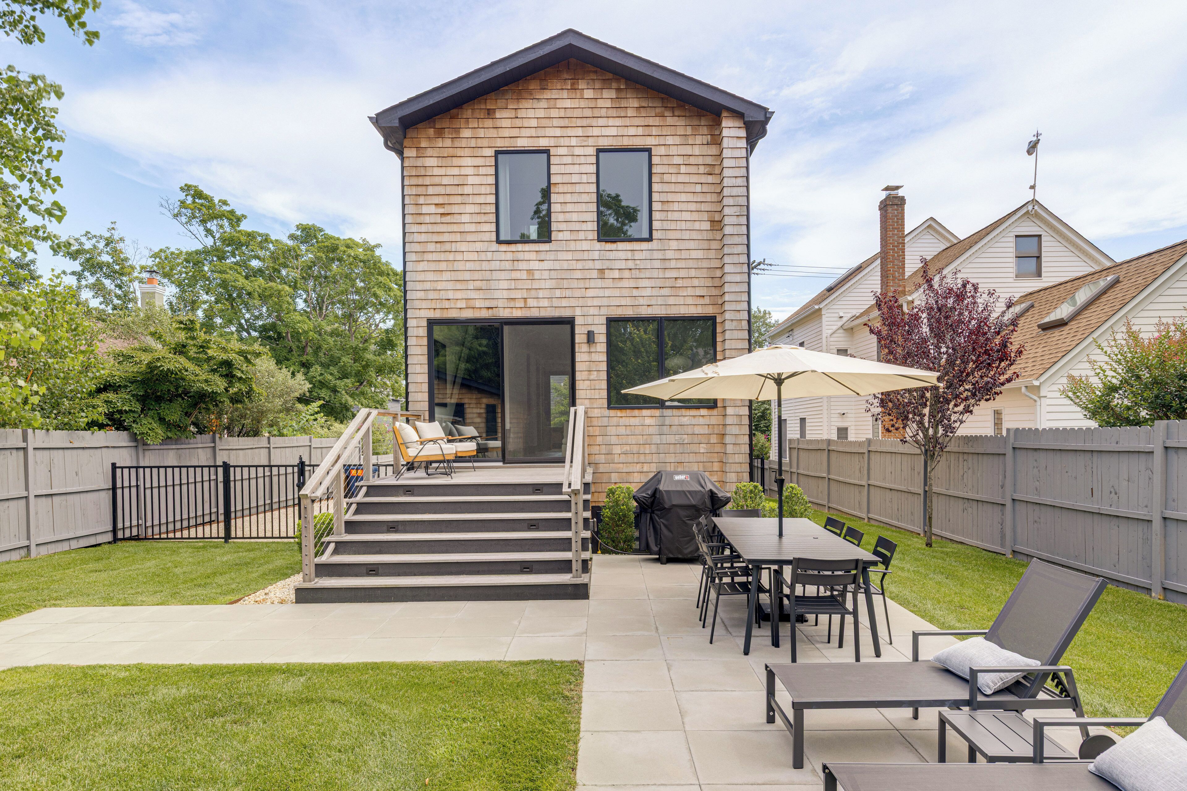 A two-story house with a patio area featuring outdoor furniture, a barbecue grill, and a covered seating area.