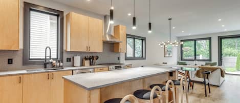 A modern kitchen with wooden cabinets, a central island with bar stools, and pendant lighting.