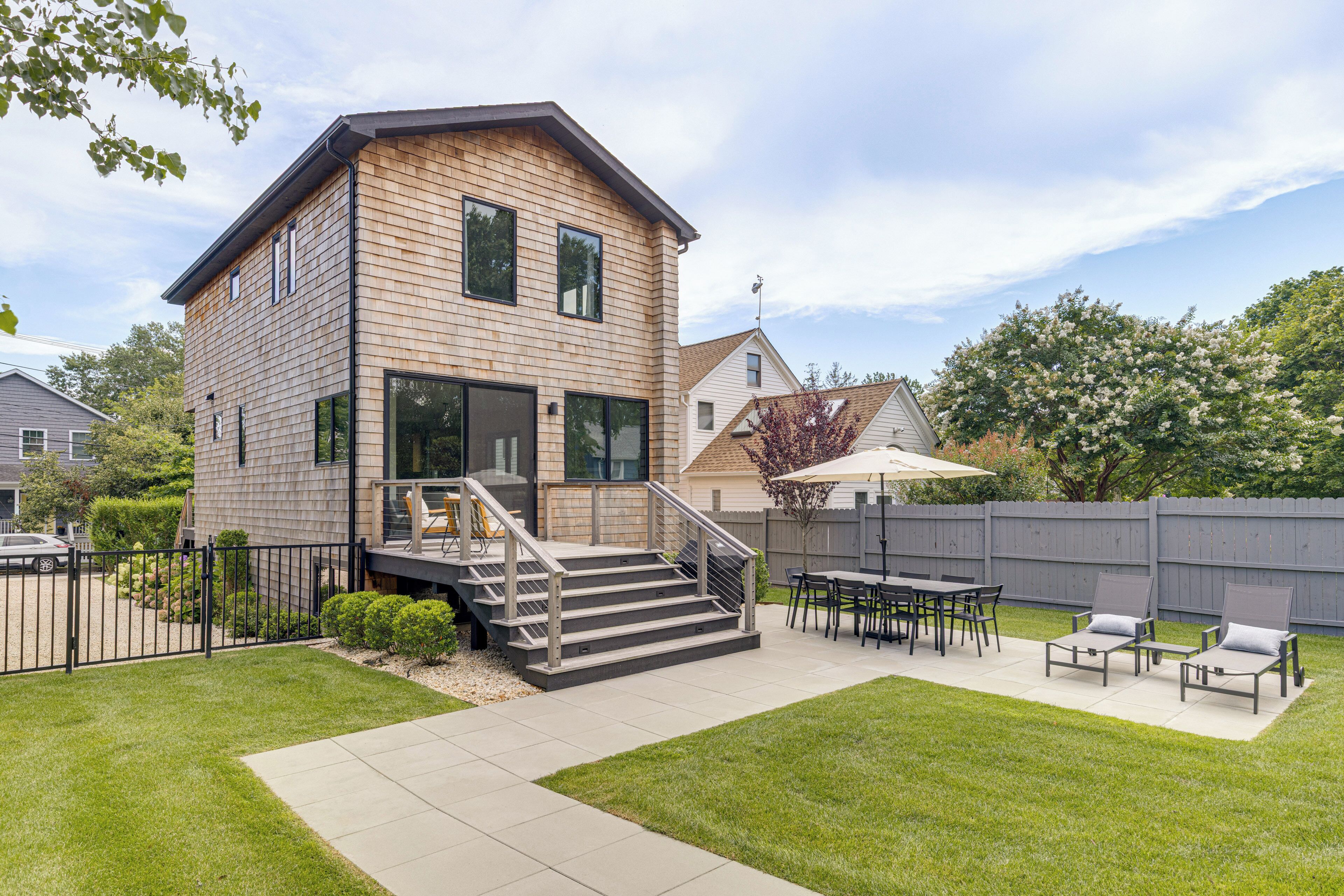 A two-story house with a deck, outdoor seating, and a fenced backyard.