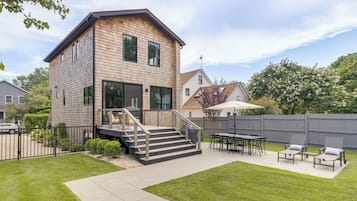 A two-story house with a deck, outdoor seating, and a fenced backyard.
