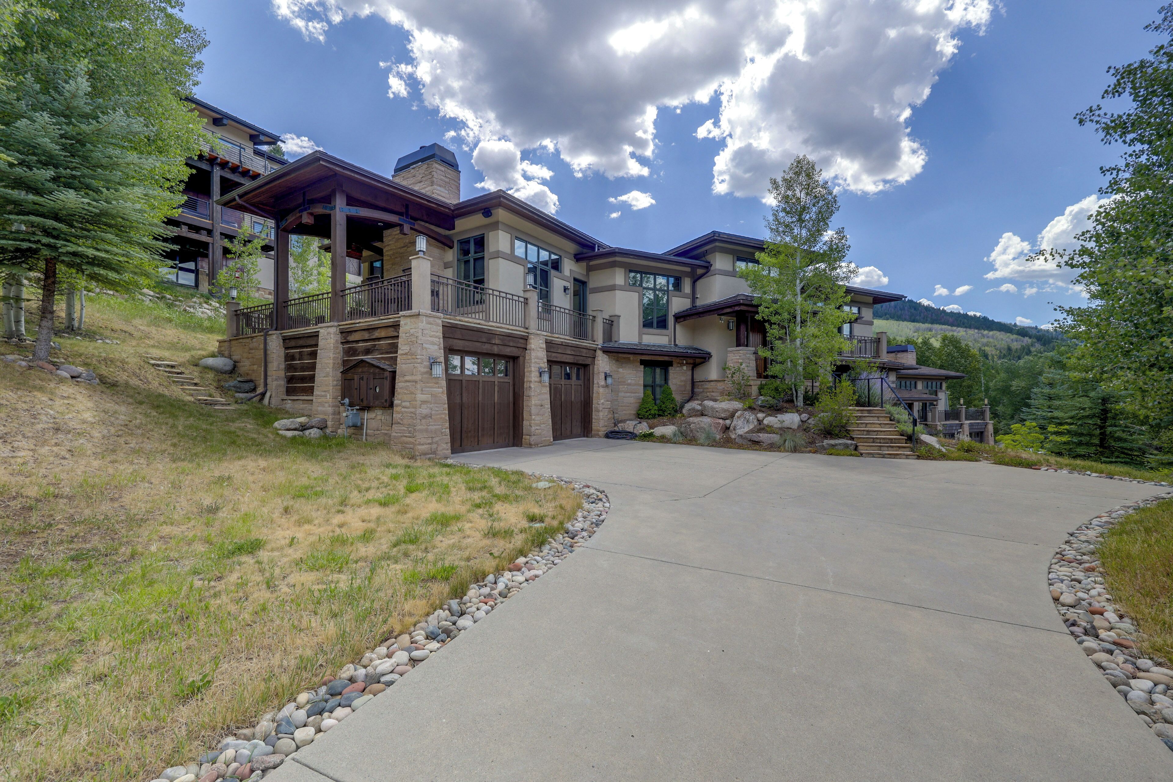 A multi-story house with a stone facade, a covered porch, and a driveway leading to the entrance.