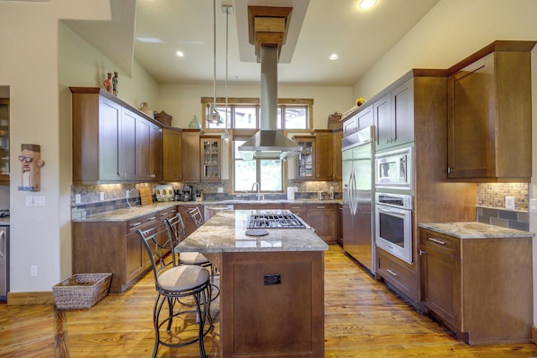 A spacious kitchen with wooden cabinets, a central island, bar stools, and modern appliances.