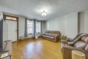 Uma sala de estar com um sofá de couro marrom, piso de madeira e teto com padrão quadriculado.