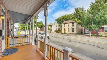 A covered porch with wooden railings, a street view with parked cars, and residential buildings.