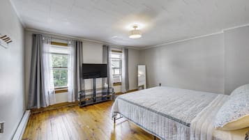 Ein Schlafzimmer mit Holzboden, einem Bett mit gemustertem Überwurf, einem Flachbildfernseher auf einem Schrank und einem Fenster mit Vorhängen.
