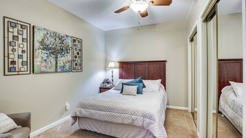 A bedroom with a bed, a ceiling fan, a nightstand with a lamp, and two framed artworks on the wall.