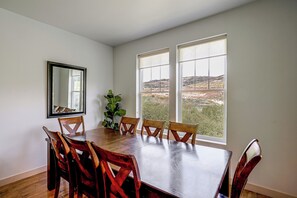Ein Esszimmer mit Holztisch, sechs Stühlen, einem Topfpflanzen und zwei großen Fenstern mit Blick auf eine hügelige Landschaft.