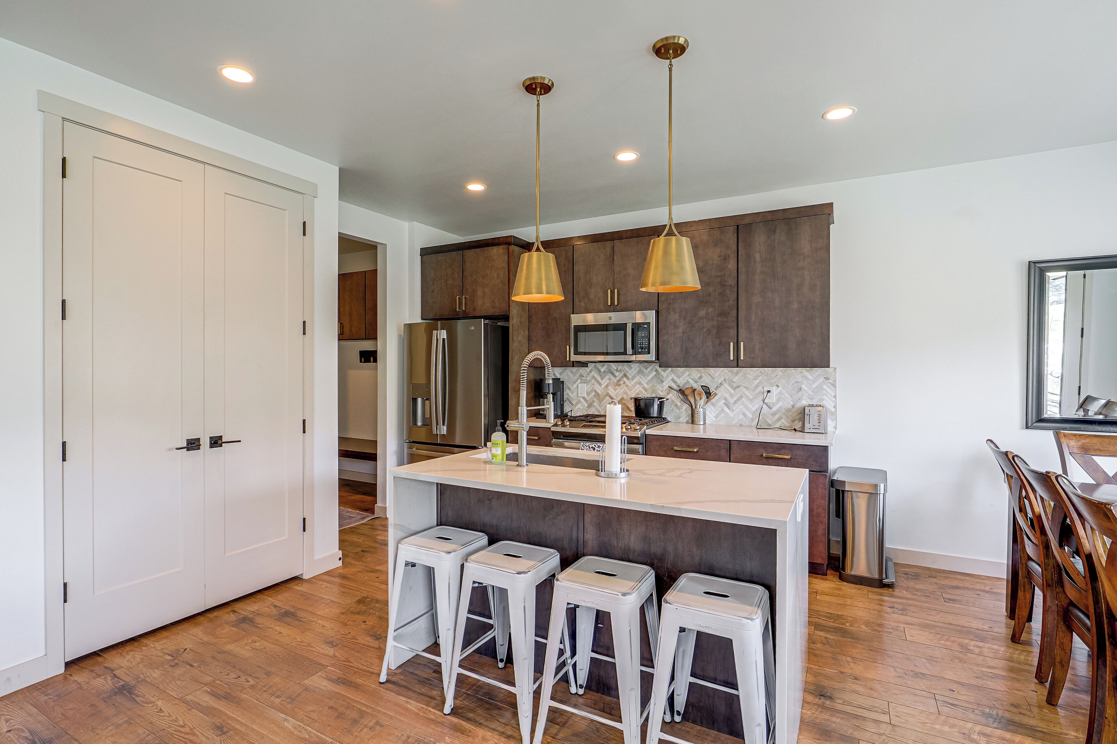 A modern kitchen with a central island, bar stools, stainless steel appliances, and pendant lighting.
