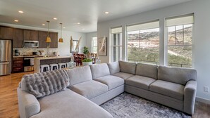 A modern kitchen with stainless steel appliances, a dining area with a large window, and a grey sectional sofa. - Hot Tub, Mtn & Lake Views! Group Abode in Daniel (Heber City)