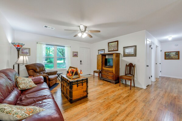 A living room with a leather sofa, a wooden cabinet, a television, and a ceiling fan.