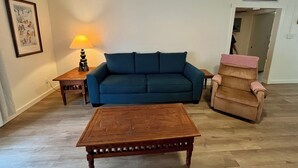 A living room with a blue sofa, a wooden coffee table, a lamp, and a chair with a pink cover.
