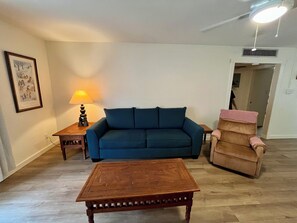 A living room with a blue sofa, a wooden coffee table, a lamp, and a chair with a pink cover.