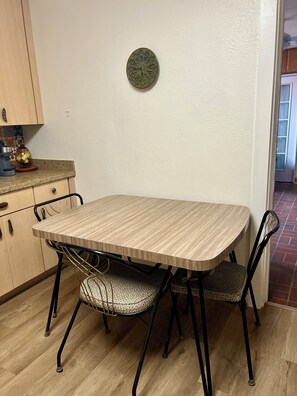 A dining table with four chairs, a coffee maker, and a decorative plate on the wall.