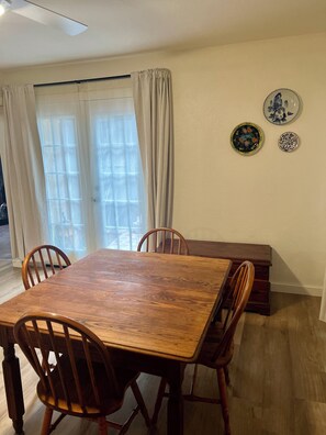 A dining area with a wooden table and chairs, a sliding glass door with curtains, and two decorative plates on the wall.