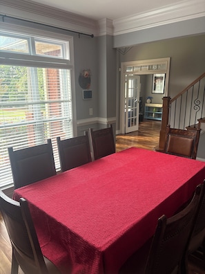 Comedor con mantel rojo, sillas de madera y vistas al exterior a través de amplios ventanales.