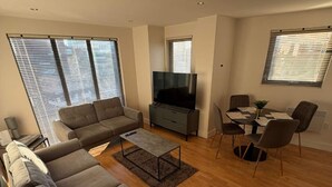 Ein modernes Wohnzimmer mit Sofa, Fernseher, Esstisch und Stühlen.