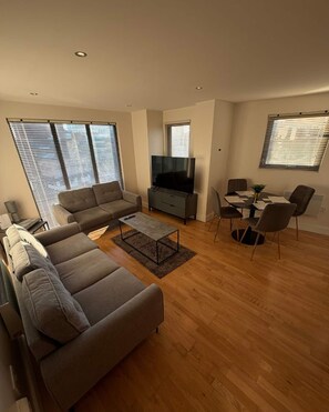 Ein modernes Wohnzimmer mit Sofa, Fernseher, Esstisch und Stühlen.