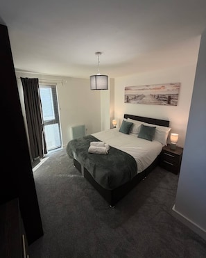 A bedroom with a bed, bedside lamps, a window with curtains, and a wall-mounted artwork. - Stylish 2-Bed w/ Balcony | City Centre (Liverpool)
