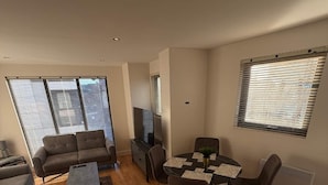 Ein modernes Wohnzimmer mit einer Couch, einem Couchtisch, einem Fernseher und einem Essbereich mit Stühlen und einem Tisch.