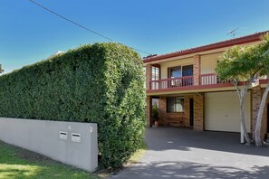 A two-story house with a balcony, a garage, and a well-maintained hedge. - The Beach Garden at Fingal Bay (Fingal Bay)