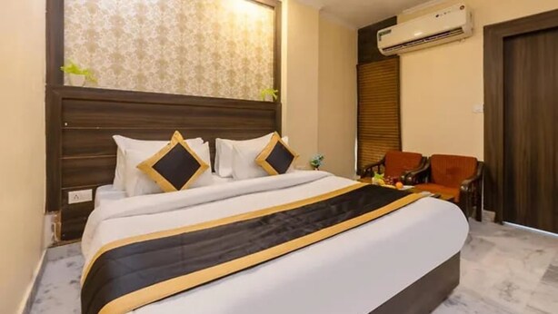 Ein Hotelzimmer mit einem großen Bett, einem Holzkopfschild, einer Klimaanlage, einem kleinen Tisch mit Stuhl und einem Fenster mit Jalousien.