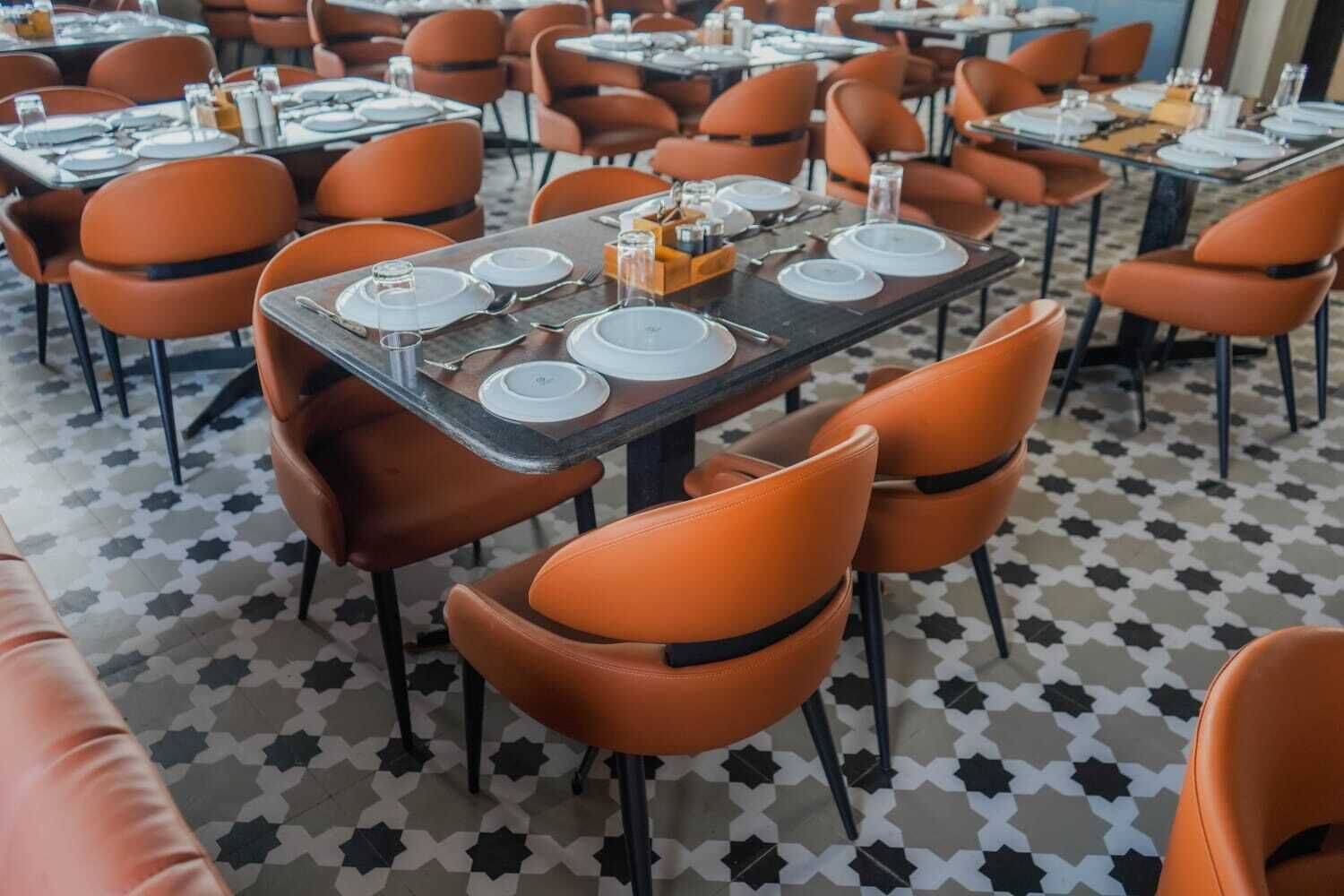 A restaurant interior with tables set for dining, orange chairs, and a patterned floor.