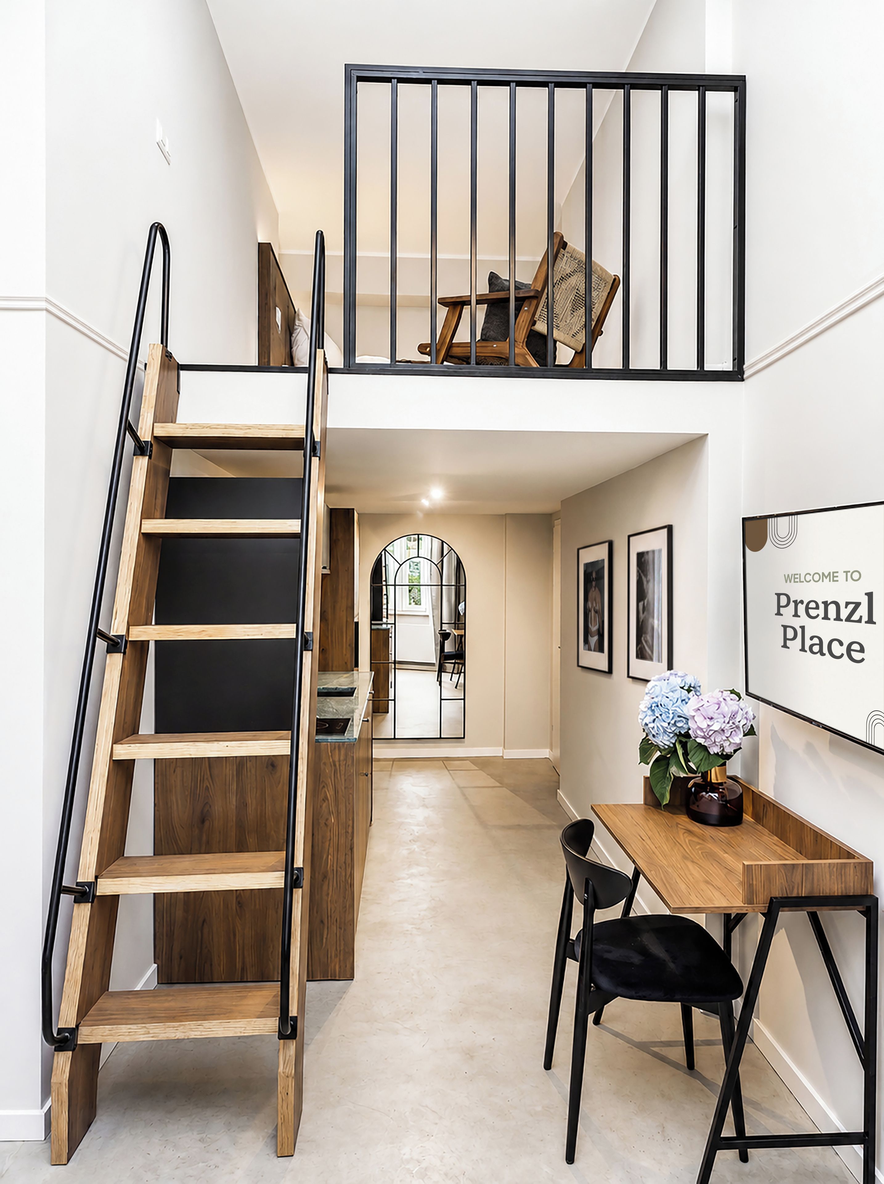 Un intérieur moderne avec un escalier en bois, un coin repas comprenant une table et des chaises, et une enseigne sur laquelle on peut lire : « Bienvenue à Prenzl Place ».