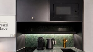 A kitchen with a black microwave, a coffee maker, and a sink with a green backsplash.
