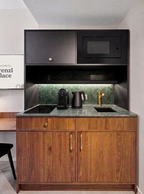 A kitchen with a black microwave, a coffee maker, and a sink with a green backsplash. - Prenzl Place (Berlin)