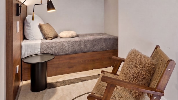 Un dormitorio con cama, mesita de noche, lámpara, silla y alfombra.