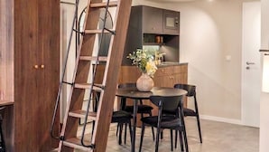 Un apartamento estilo loft con escalera de madera, un comedor con mesa y sillas redondas, y una kitchenette.
