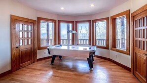 Ein Zimmer mit Billardtisch, großen Fenstern, Holztüren und einer Decke mit eingelassener Beleuchtung.