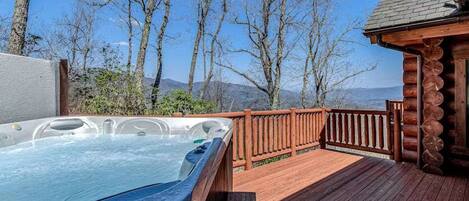 A hot tub on a wooden deck with a view of trees and mountains.