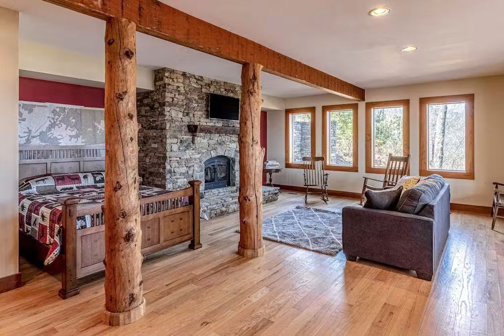 A spacious living area with a stone fireplace, wooden beams, a sofa, and a bed with a quilt.