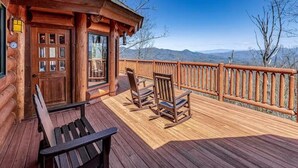 Eine Holzterrasse mit einer Bank und zwei Schaukelstühlen, mit Blick auf eine gebirgige Landschaft.