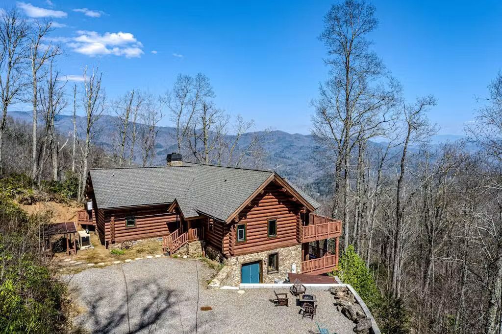 A log cabin with a balcony, a stone entrance, and a patio area with outdoor seating.
