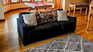 Ein Raum mit einem dunkelgrauen Sofa, einem Billardtisch und einem Kicker.