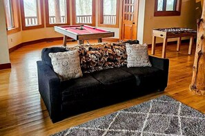 A room with a dark-colored sofa, a pool table, and a foosball table. - Two Bears | Mountain Views and Game Nights (Franklin)