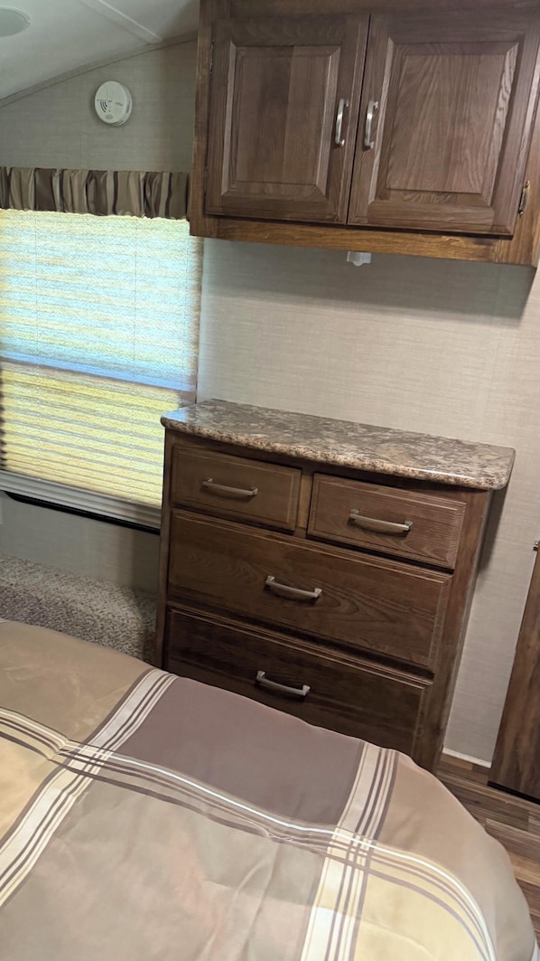 Un dormitorio con cama, cómoda de madera y ventana con persianas.