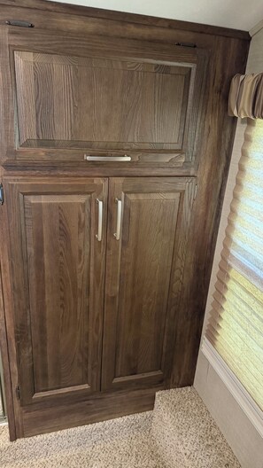 Een grote houten kast met twee deuren en een lade, geplaatst tegen een muur met een raam.