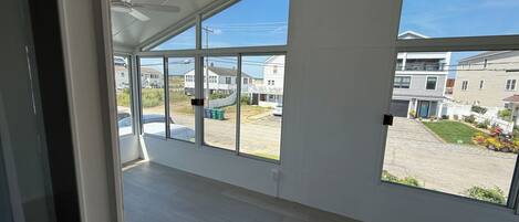 Une pièce spacieuse avec de grandes fenêtres, un ventilateur de plafond et une vue sur un quartier résidentiel.