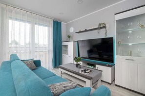 A modern living room with a sofa, coffee table, TV, and a glass cabinet with decorative items. - Spacious Apartment with Air Conditioning | Desk | Balcony (Katowice)