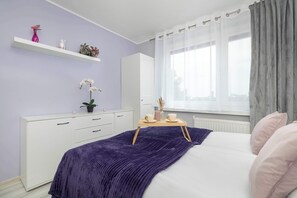 A bedroom with a bed, a dresser, a window with curtains, and a shelf with decorative items. - Spacious Apartment with Air Conditioning | Desk | Balcony (Katowice)