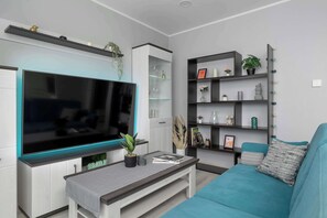 Ein modernes Wohnzimmer mit einem großen Flachbildfernseher, einem türkisfarbenen Sofa und einem Bücherregal mit Dekoration.