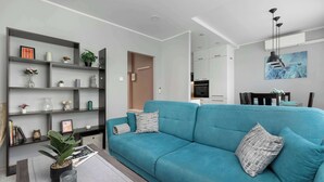 Ein modernes Wohnzimmer mit einem türkisfarbenen Sofa, einem Bücherregal und einem Essbereich mit Tisch und Stühlen.