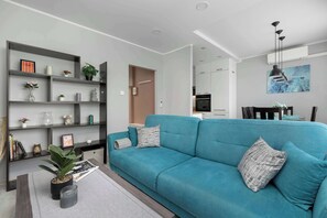 A modern living room with a teal sofa, a bookshelf, and a dining area with a table and chairs. - Spacious Apartment with Air Conditioning | Desk | Balcony (Katowice)