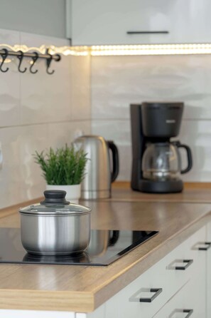 A kitchen with a stainless steel pot on an induction cooktop, a coffee maker, and a potted plant. - Spacious Apartment with Air Conditioning | Desk | Balcony (Katowice)