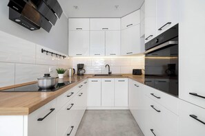 A modern kitchen with white cabinets, a wooden countertop, a built-in oven, and a black range hood. - Spacious Apartment with Air Conditioning | Desk | Balcony (Katowice)